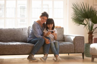 Mutlu anne ve çocuk kızı kanepede oturan smartphone kullanarak