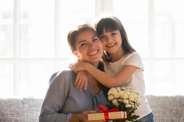 Happy kid daughter embracing mom holding flowers bouquet and gift — Stock Photo, Image
