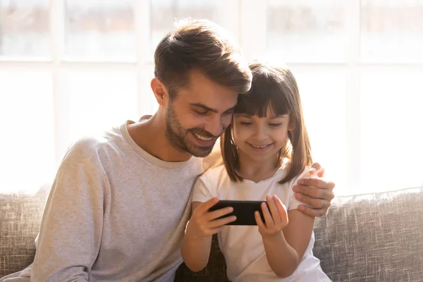 Счастливый папа и маленькая девочка держат телефон с помощью смартфона — стоковое фото