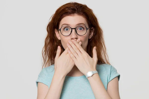 Chockad Rödhuvad kvinna som tittar på kameran som täcker munnen med händerna — Stockfoto
