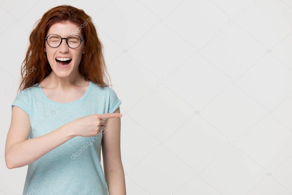 Cheerful red-haired woman laughing pointing at funny advertisement copy space