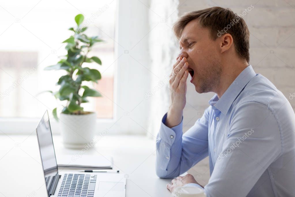 Businessman yawning in the office while working with laptop 