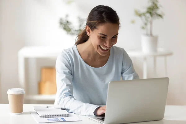 Веселая женщина смешанной расы улыбается печатая на компьютере — стоковое фото