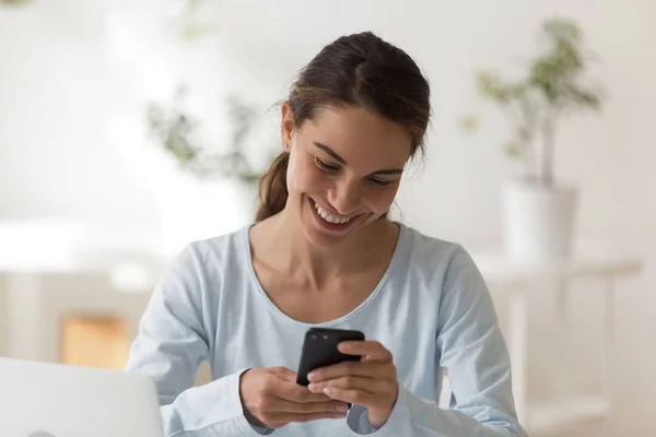 Alegre hembra sentada en la mesa leyendo el mensaje usando el teléfono — Foto de Stock