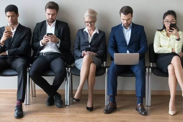 Различные бизнесмены, сидящие в ряд с помощью устройств телефонов и ноутбуков — стоковое фото