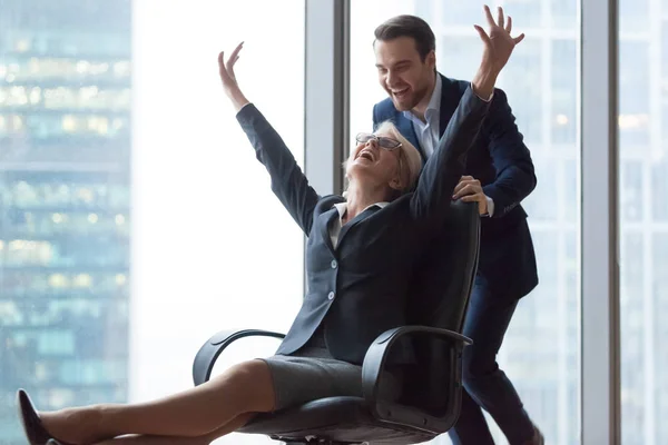 Happy carefree middle-aged businesswoman enjoying office activity riding on chair