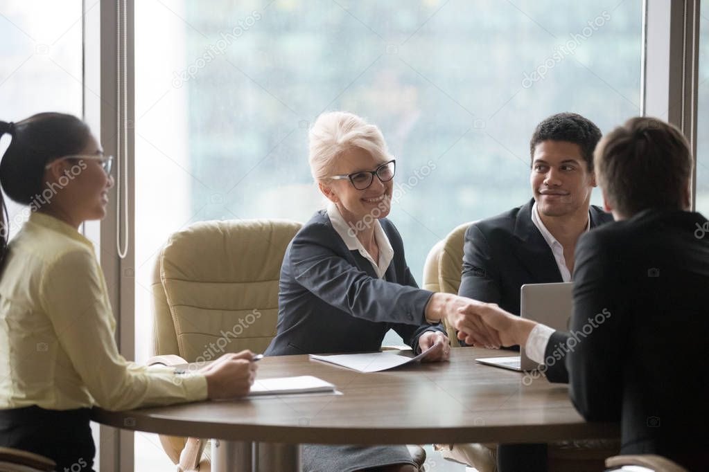 Happy businesswoman handshaking businessman over conference table at team meeting