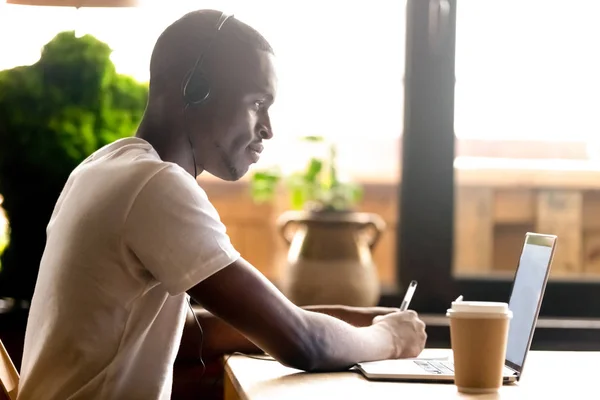 Чёрный студент учится с помощью ноутбука и наушников — стоковое фото