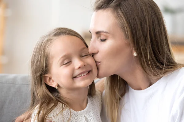 Kärleksfull ung mamma kysser lilla leende dotter på kinden — Stockfoto