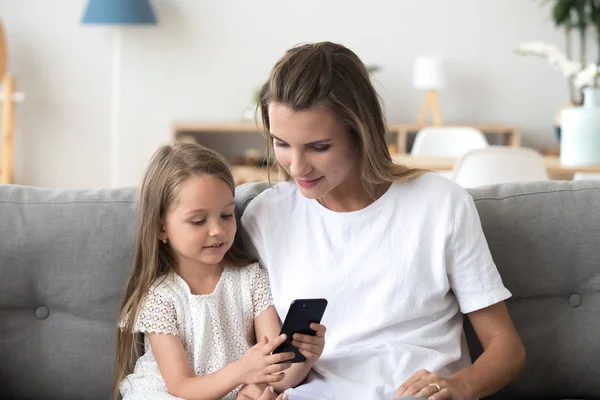 Menina com a mãe usando o telefone juntos em casa, se divertindo — Fotografia de Stock