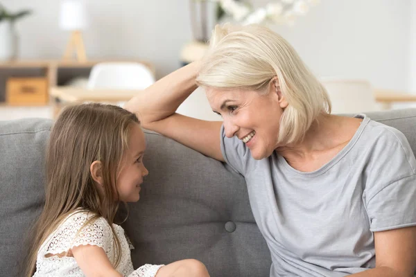 Nieta pequeña hablando con la abuela atenta, sentada en el sofá — Foto de Stock