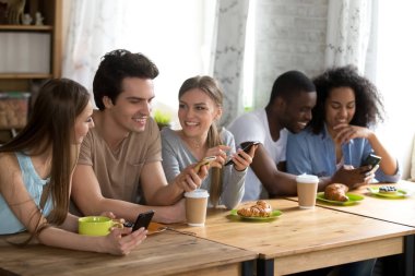 Telefonunu kullanarak birlikte kafede oturan mutlu gülümseyen arkadaşlar