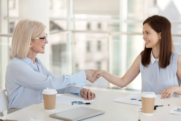 Счастливые деловые женщины разных возрастов пожимают друг другу руки в офисе — стоковое фото