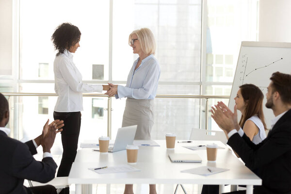 Пожилая женщина-босс пожимает руку продвинутому работнику
