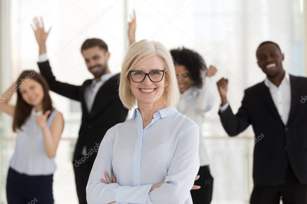 Aged confident team leader with coworkers posing looking at camera