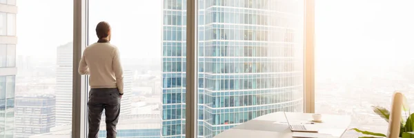 Horizontal image rear view businessman standing looking through panoramic window — Stock Photo, Image