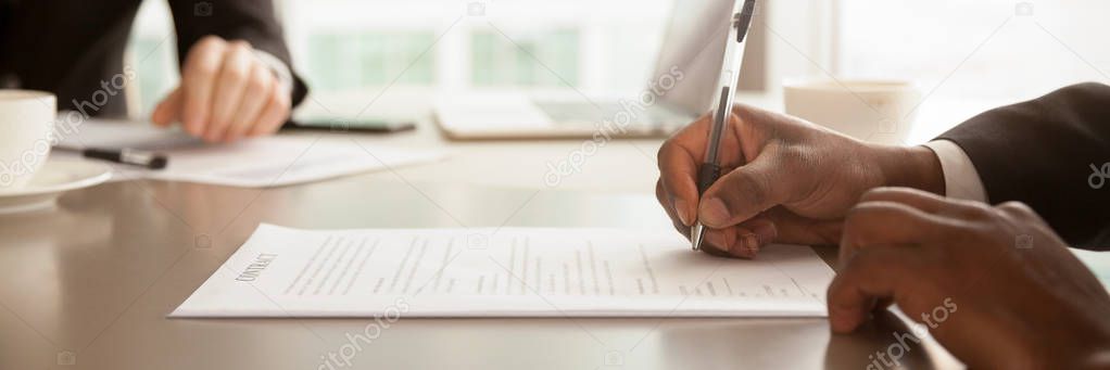 Horizontal close up photo african businessman sitting at desk holds pen signing contract paper, lease mortgage, employment hr or affirm partnership agreement concept, banner for website header design