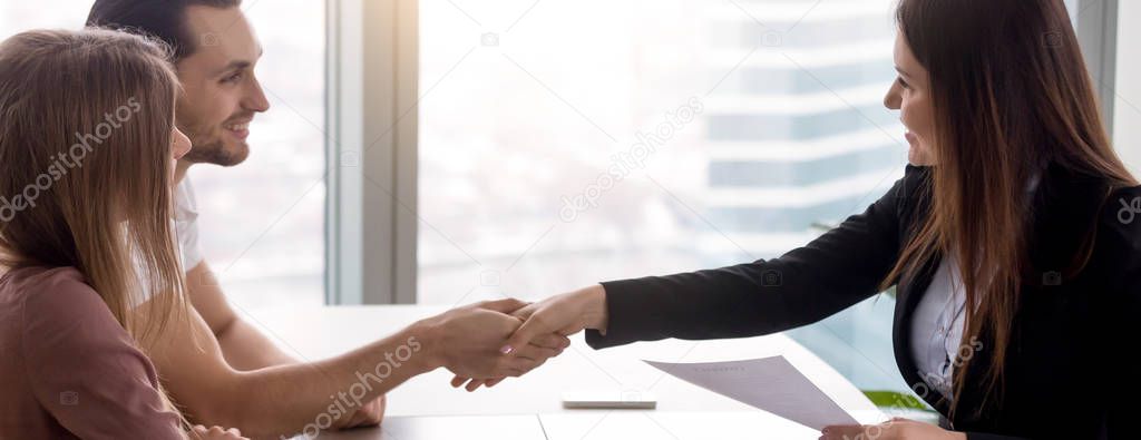Horizontal image couple signing real estate contract handshaking with realtor 