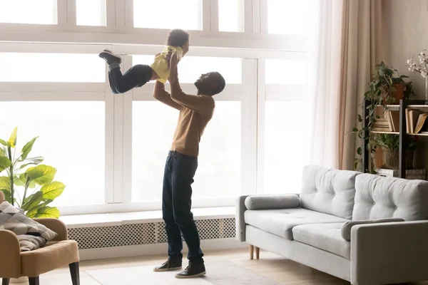 Feliz africano papá lifting pequeño niño hijo jugando en casa —  Fotos de Stock