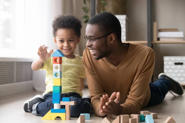 Pequeno filho feliz brincando com o pai preto usando blocos de madeira — Fotografia de Stock