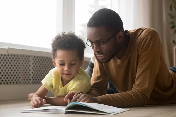 Gelukkig zwarte vader en peuter zoon lezen boek thuis — Stockfoto