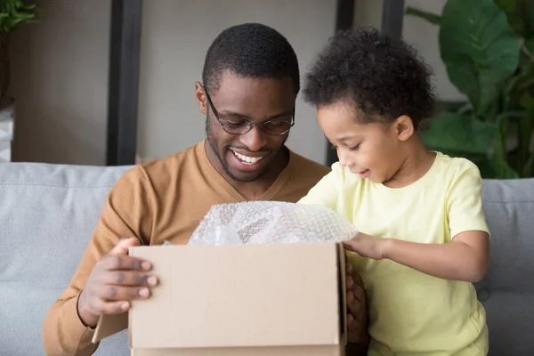 Feliz pai negro e filho pequeno caixa de papelão aberta — Fotografia de Stock