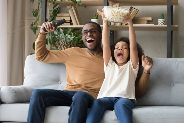 Feliz padre negro lleno de alegría con hija niño viendo la televisión juego —  Fotos de Stock