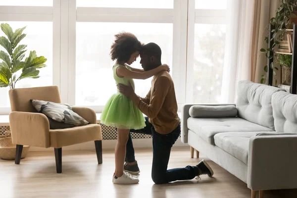 Люблячий чорний тато обіймає дівчинку, що стоїть на коліні — стокове фото