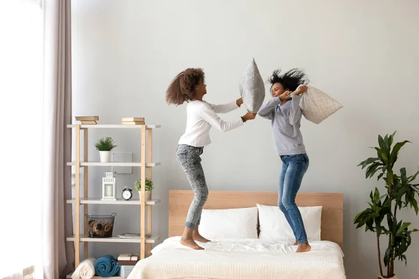 Mãe e filha africana desfrutando de travesseiro luta pulando na cama — Fotografia de Stock