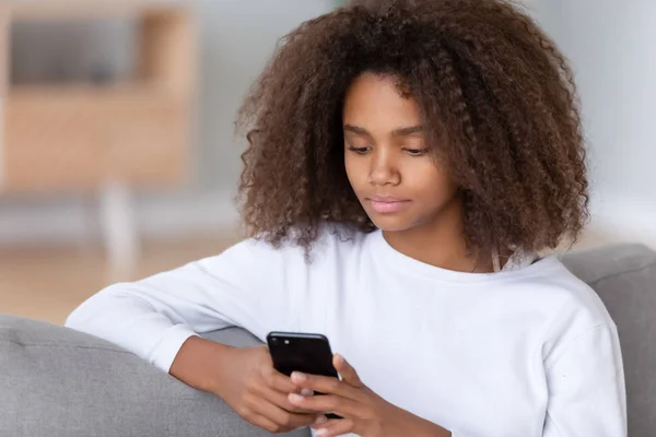 Tutup african gadis remaja duduk di sofa menggunakan smartphone — Stok Foto