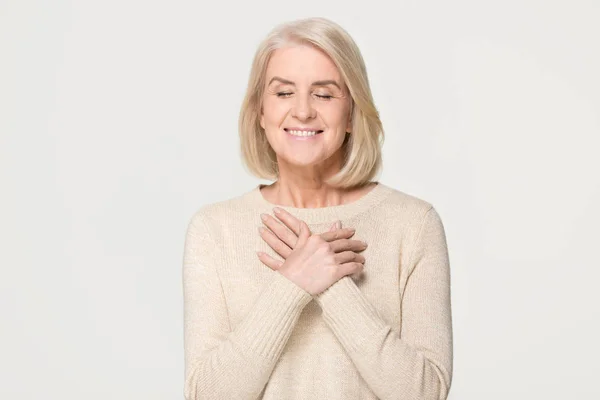 Dankbar reife Frau hält Hände auf Brust isoliert auf dem Hintergrund — Stockfoto