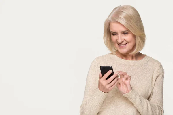 Glad mogen senior kvinna med smartphone isolerad på grå bakgrund — Stockfoto
