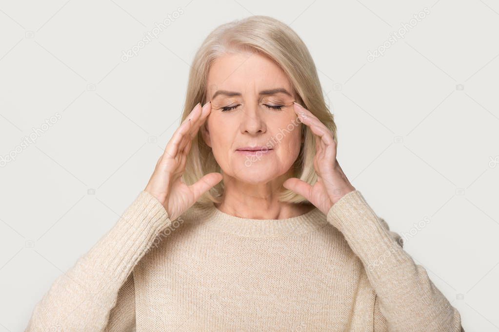 Calm healthy old woman massaging temples feeling stress relief