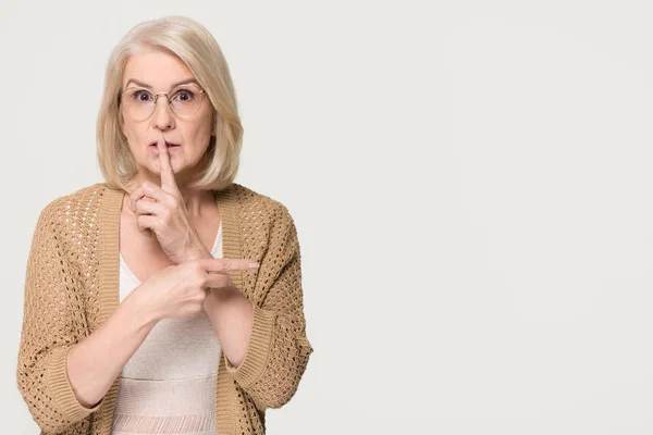 Old woman holding finger on lips pointing at copyspace isolated — Stock Photo, Image