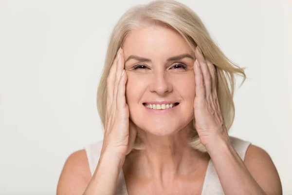 Happy zralá žena dotýká tvář izolovaná proti stárnutí beauty koncept — Stock fotografie