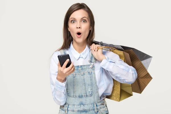 Förvånad tjej håller väskor telefonen överraskad av app shopping försäljning — Stockfoto