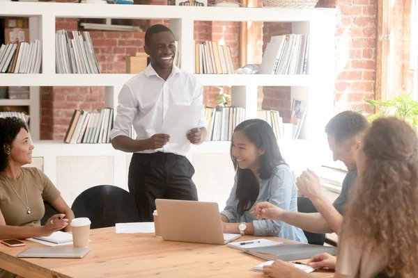 Sonriente líder negro sosteniendo informe de papel riendo con diverso equipo — Foto de Stock