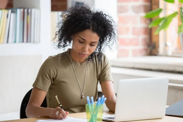 Lavoratrice o studentessa africana che lavora con il computer portatile prendendo appunti — Foto Stock