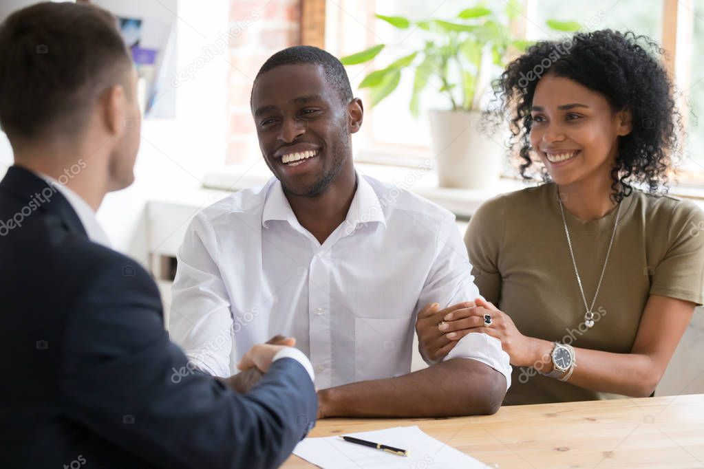 Happy black couple handshaking realtor insurer landlord at meeting