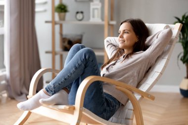 Eğilerek geri sandalyede rahat evde rahatlatıcı gülümseyen genç kadın