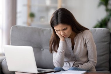 Bored unmotivated woman sitting at table with laptop and documents clipart