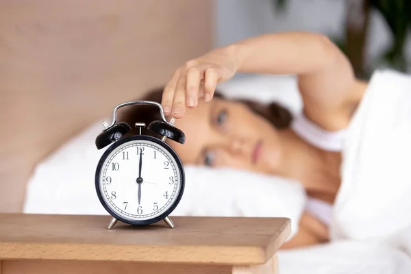 Wanita muda berbaring di tempat tidur, dibangunkan oleh sinyal alarm, mematikan jam — Stok Foto