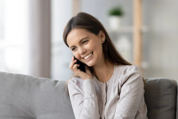 Mujer joven sonriente hablando por teléfono, sentada en el sofá en casa —  Fotos de Stock
