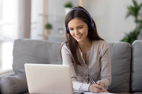 Smiling woman in headphones using laptop, writing notes — Stock Photo, Image