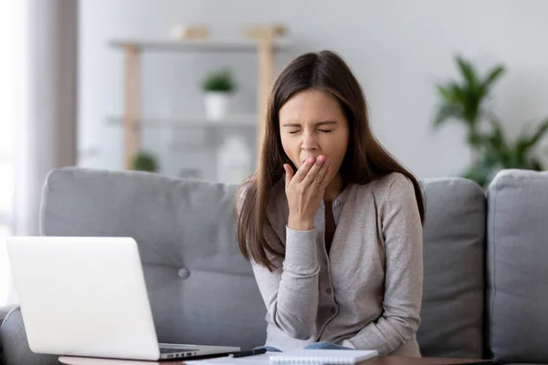 Уставшая женщина зевает, сидит за столом с ноутбуком, ленивая на работе — стоковое фото