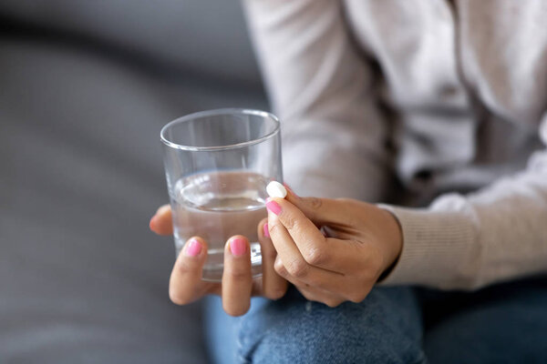Close up sick woman holding glass with water and pill in hands