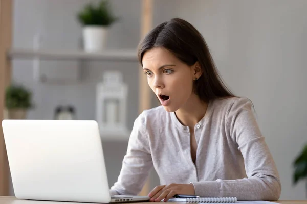 Förvånad ung kvinna med öppnade munnen tittar på laptop skärmen — Stockfoto