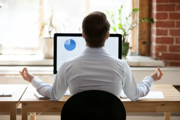 Rear view businessman sitting at desk opposite pc doing yoga — Stock Photo, Image