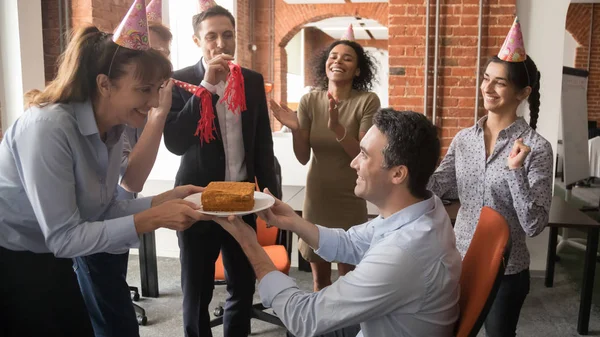 Friendly diverse employees in party hats presenting cake congratulating colleague