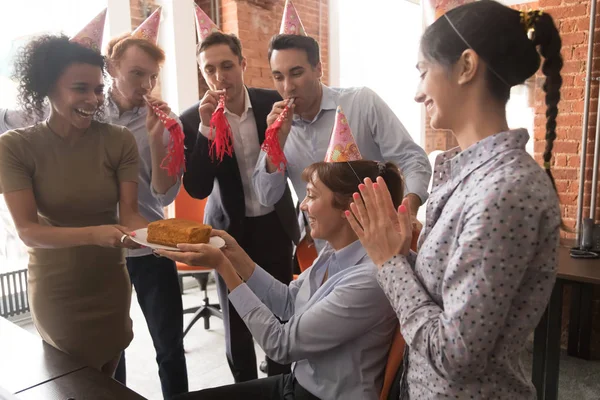 Multicultural employees in party hats congratulate female with birthday cake